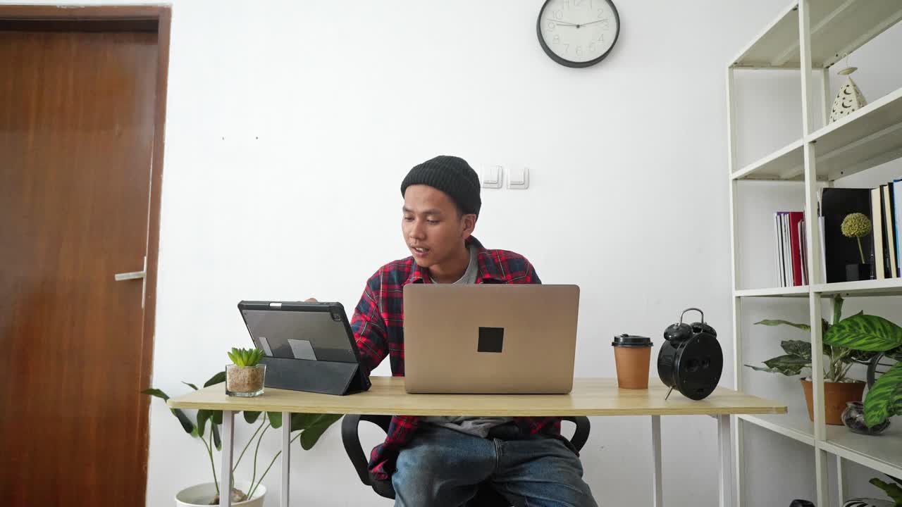 Young Asian Man Busy Working Using Laptop And Tablet At Home