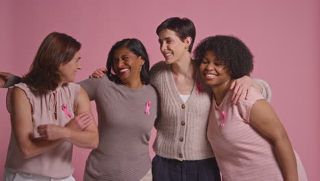 Studio-Portrait-Of-Multi-Racial-Group-Of-Smiling-Women-Of-Different-Ages-Wearing-Pink-Clothing-And-Breast-Cancer-Awareness-Ribbons-Hugging-Against-Pink-Background