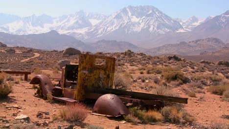 Abandoned-pickup-truck-with-the-snowcapped-Sierra-Nevada-mountains-with-the-sun-shining-through-clouds