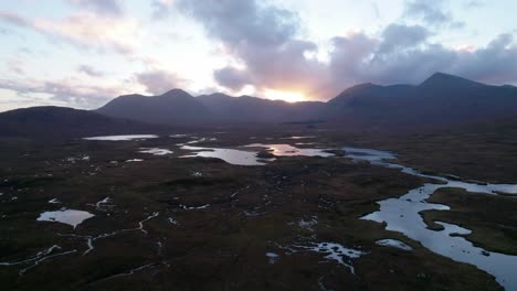 Eine-Drohne-Dreht-Sich-Langsam-Hoch-über-Einer-Torflandschaft-Aus-Torfmooren-Inmitten-Eines-Mosaiks-Aus-Süßwasserseen-Und-Blickt-Bei-Sonnenuntergang-Auf-Die-Berge-Am-Horizont