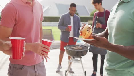 happy diverse male friends talking and drinking beer in garden on sunny day