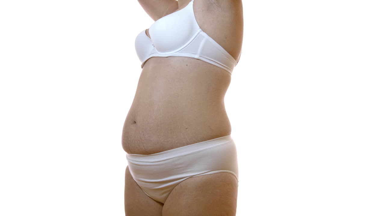 Closeup on flabby belly of female body with stretch marks over white studio background. Overweight woman wearing only white underwear presenting her skin and dermatology issues