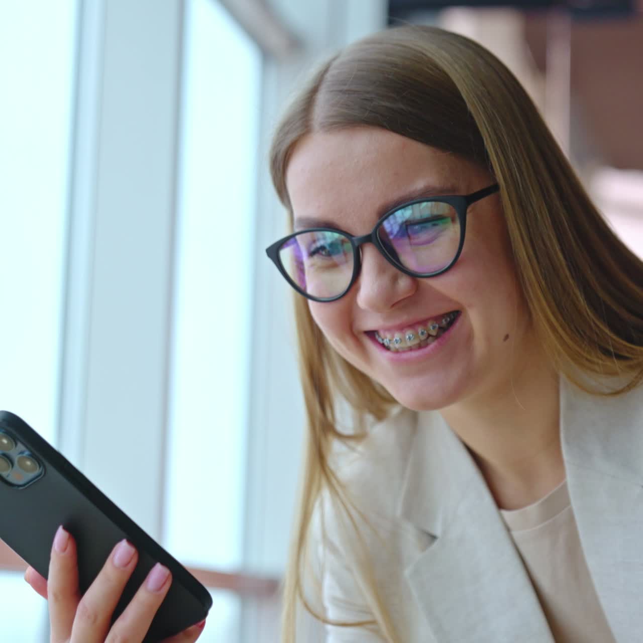 Smiley young woman speaks on the phone cheerfully. Long-haired woman in glasses bent over the screen. Close up