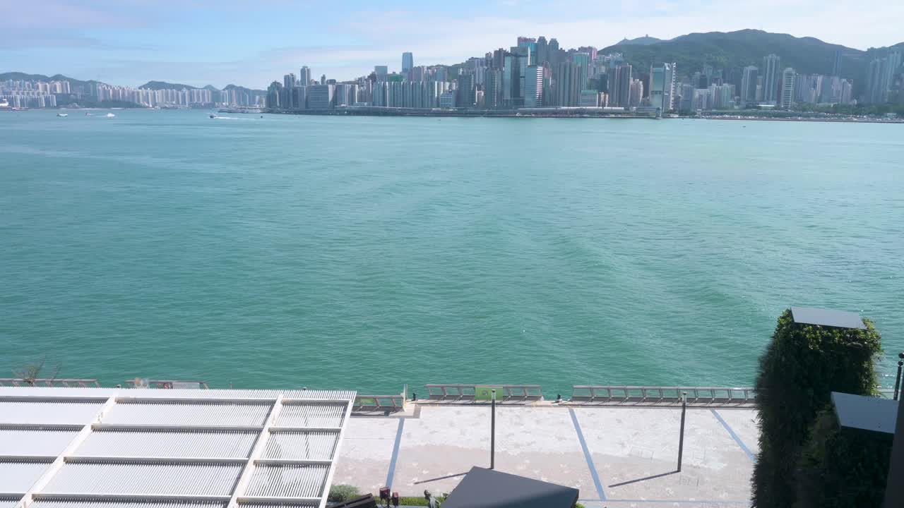 A pedestrian walks through Victoria Harbour waterfront as they enjoy their evening, sunset, and skyline view of Hong Kong Island skyscrapers