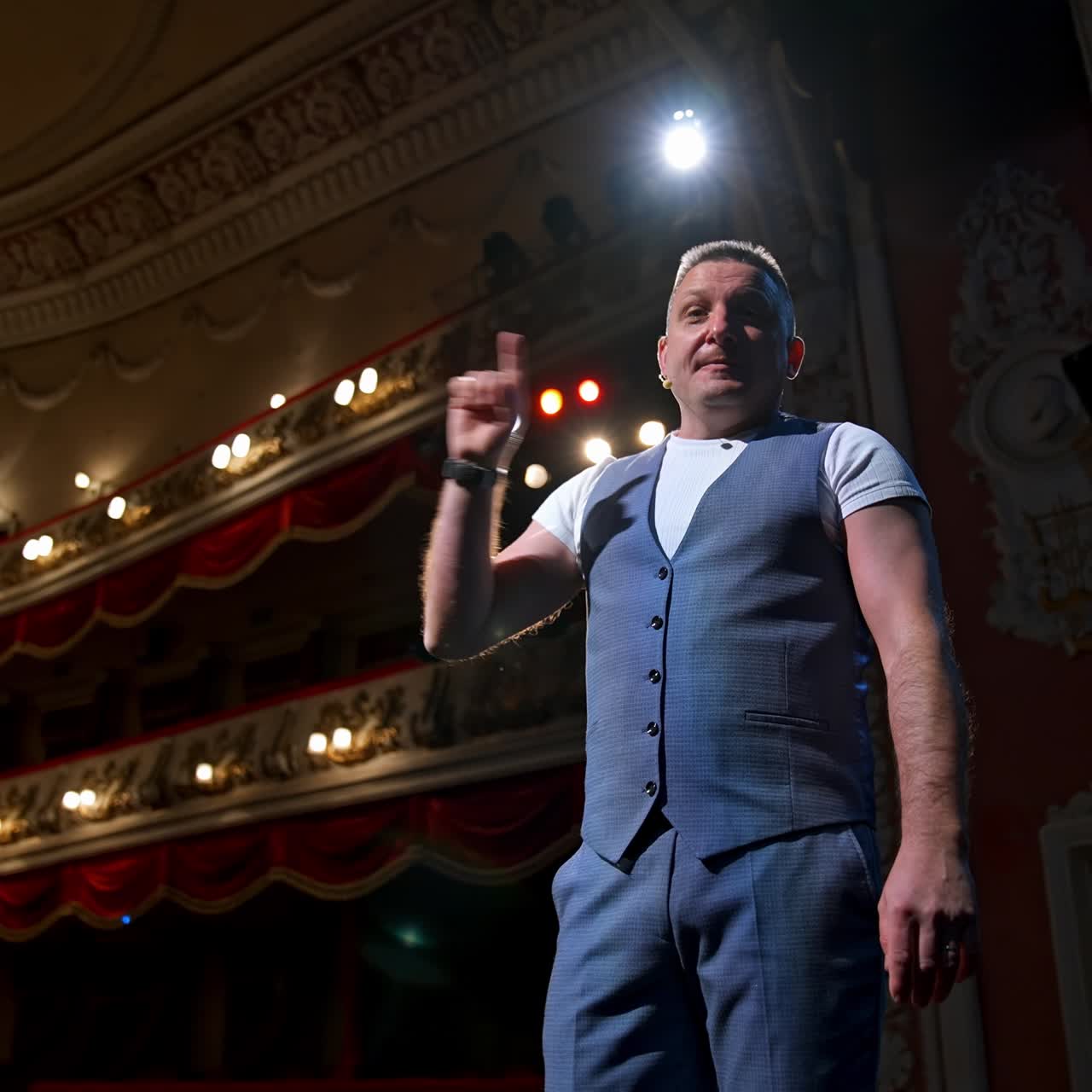 Man in front of theater hall put hand to ear. Actor is standing on stage and talking with public during the performance. Classic theater interior