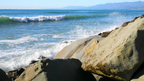 a slow motion sliding shot of large blue ocean waves crashing against the rocks on a california beach slide left