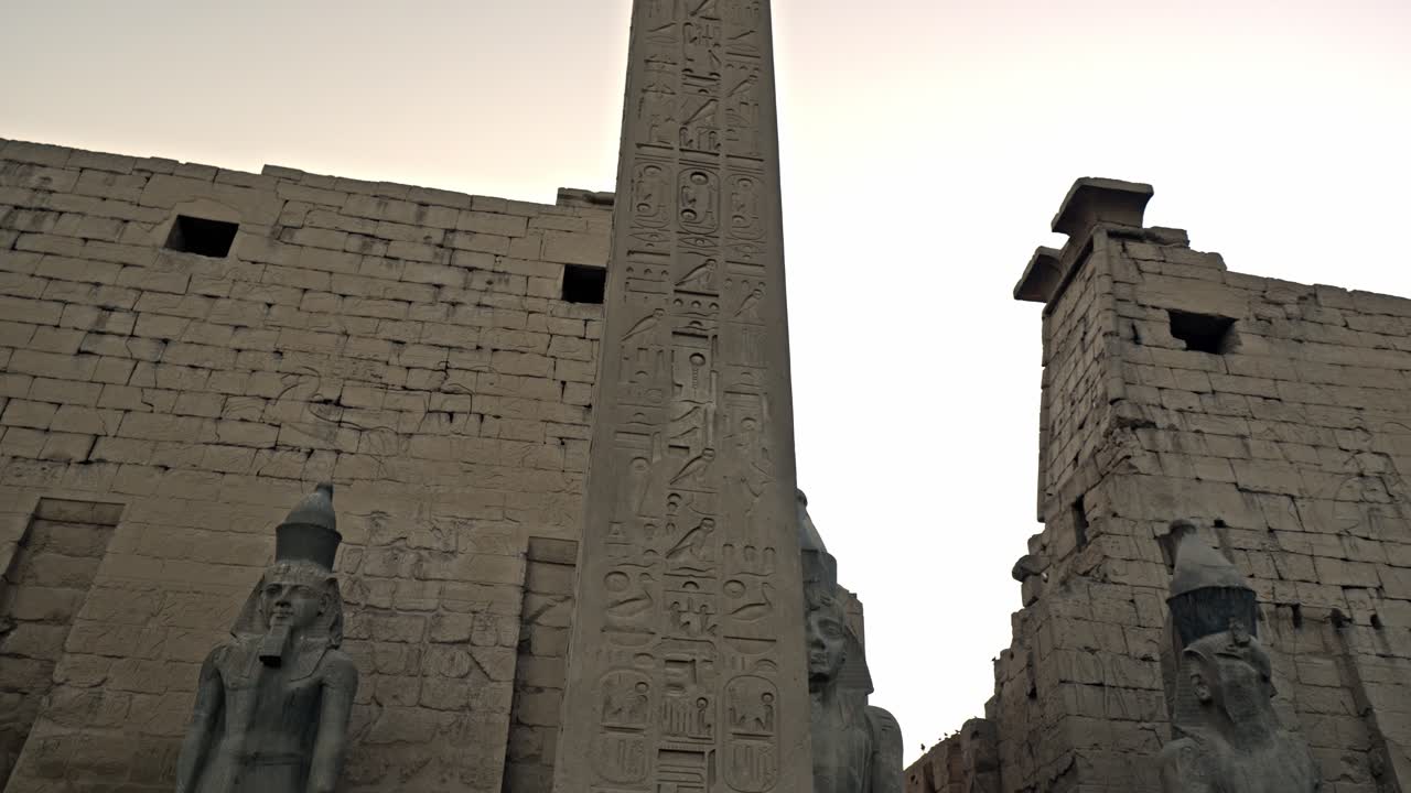 Bu manzara, tapınağın Ramses II tarafından inşa edilen devasa bir geçit olan Birinci Pilonunu göstermektedir. Pilonun önünde, orijinal çiftin bir parçası olan tek bir pembe granit dikilitaş durmaktadır.