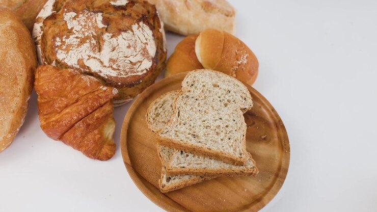 Hand reaches for sliced whole wheat bread on wooden plate amidst various artisan bakery items.