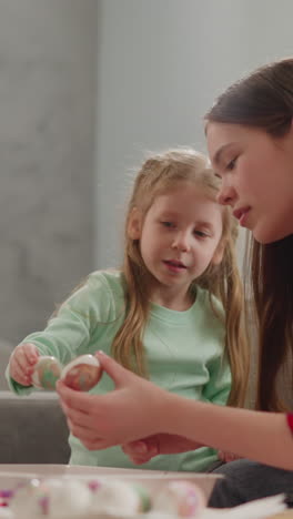 una niña bonita con una hermana mayor mira huevos de pascua con decoración abstracta de mármol en casa en cámara lenta. tendencias de celebración de vacaciones cristianas