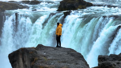orbiting on a man standing over rock cliffs near godafoss waterfall in iceland