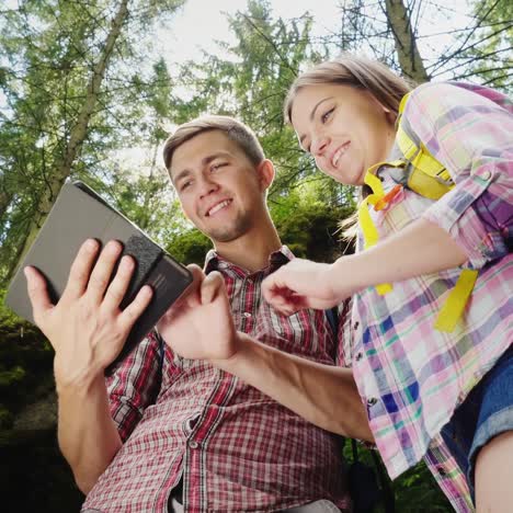 happy couple of tourists with backpacks orient themselves in the forest using a tablet