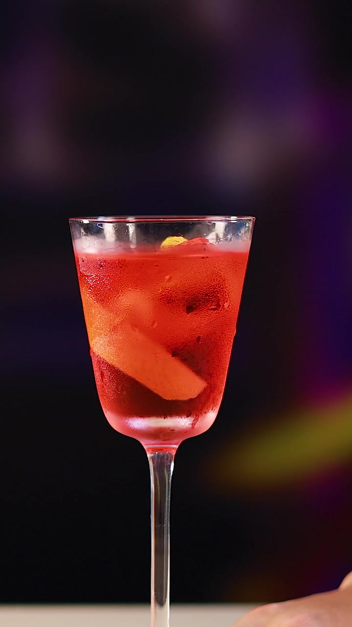 Un cóctel Negroni está sobre una barra de bar con iluminación vibrante y un fondo difuminado