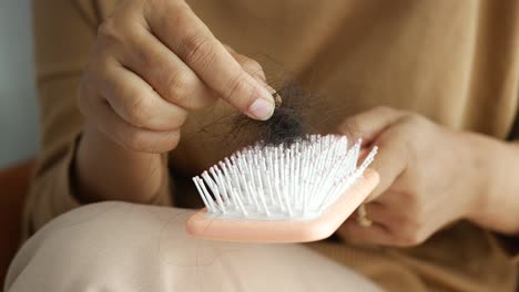 woman experiencing hair loss, plucking out hair strands from a comb