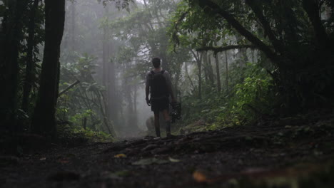 El-Hombre-Camina-Con-El-Equipo-De-La-Cámara-Por-El-Camino-De-La-Selva-Nublada,-A-Cámara-Lenta