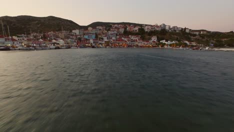 Aerial:-Small-fishing-town-with-Greek-flag-on-Samos-island,-Greece