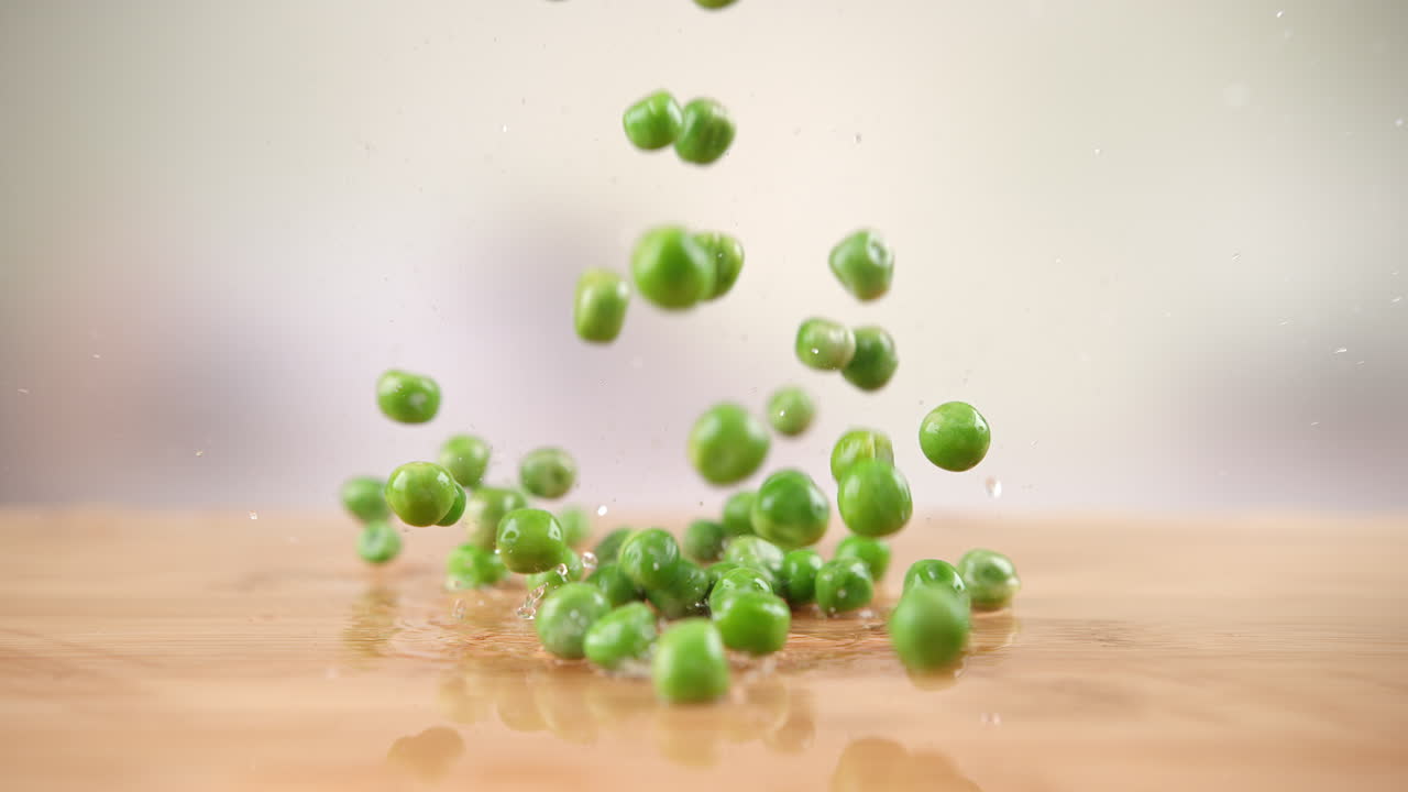 Green Peas Falling Onto The Wet Wooden Kitchen Table, Bouncing And Splashing Water Droplets around in Macro and Slow Motion