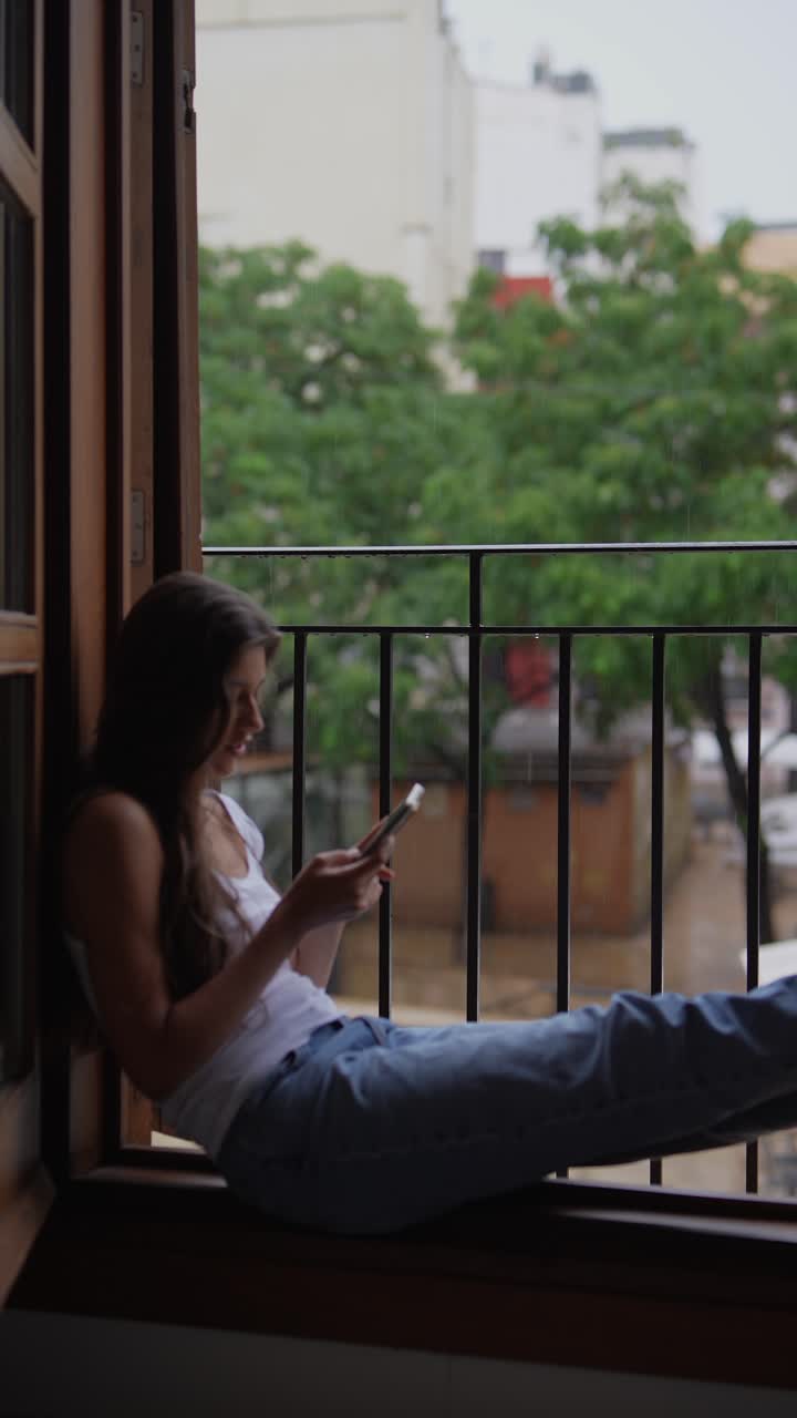 mujer usando el teléfono en el balcón lluvioso