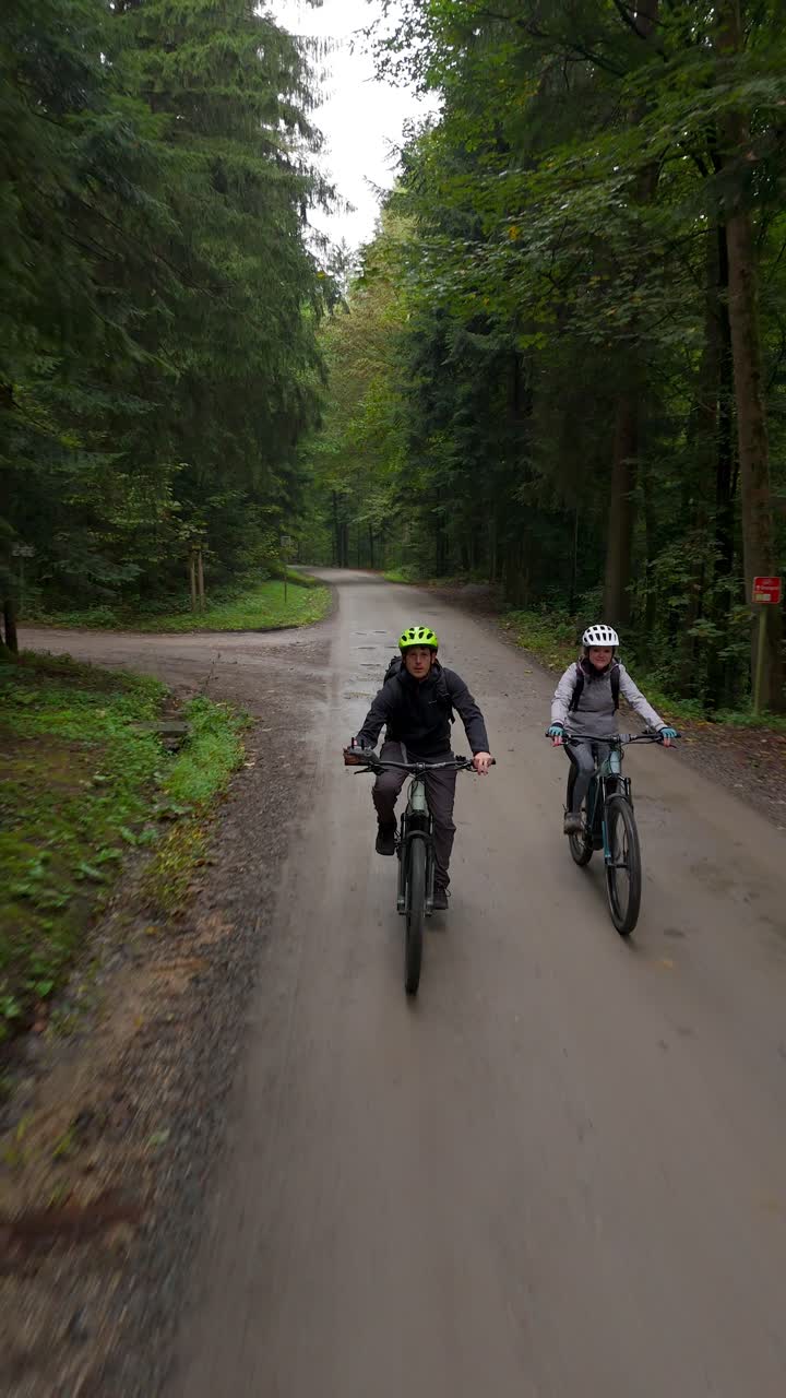 Couple Riding E-bikes Along The Towering Trees In The Forest. - aerial vertical shot