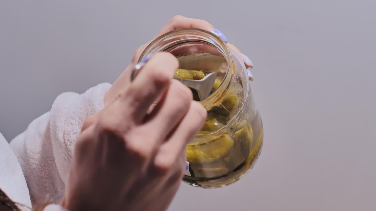 Jar opened as woman grabs crunchy pickle with fork in quiet indoor moment