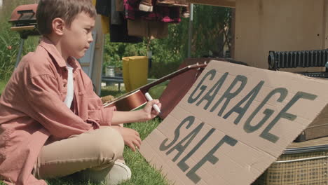 niño haciendo un letrero para la venta de garaje