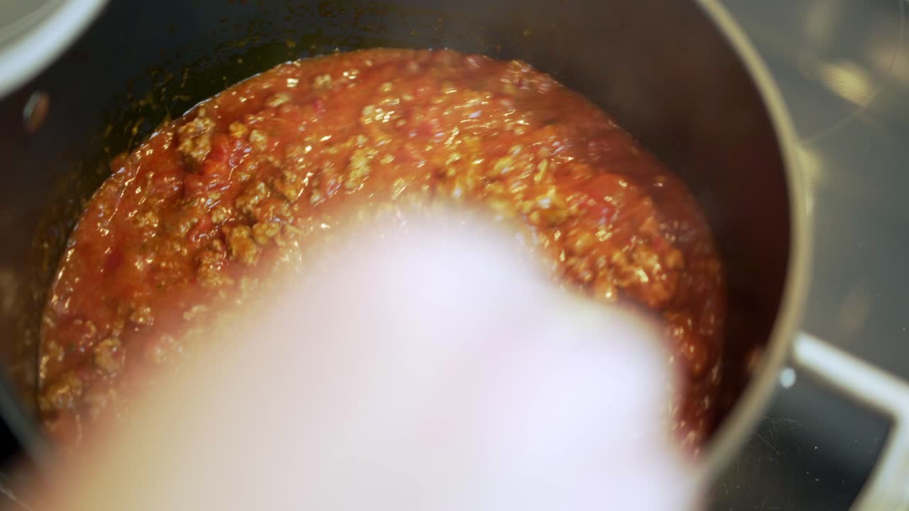 Bolognese cooking and bubbling in black po stored once then lid on pot