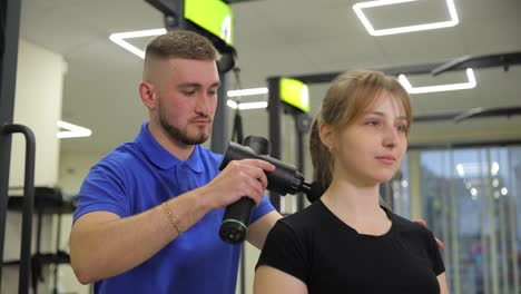 man giving woman a massage in a gym using a percussion therapy device.