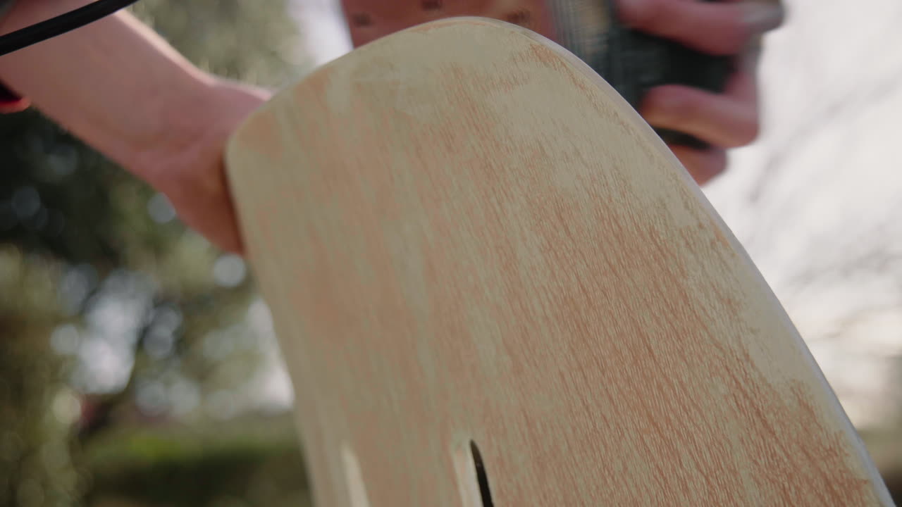 Detailaufnahme eines Handwerkers, der eine Poliermaschine benutzt, um Holz zu polieren und einen alten Vintage-Designstuhl im Garten an einem sonnigen Tag aufzuarbeiten 4K