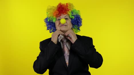 Senior-elderly-clown-businesswoman-boss-in-wig-adjusts-tie.-Yellow-background