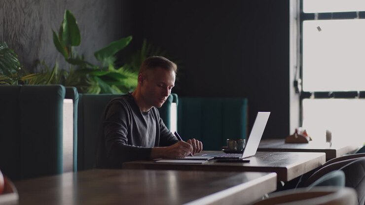 Smiling man with works from home in his kitchen using a laptop. Remote work and remote learning. remote work during self-isolation in quarantine, man works with financial documents.