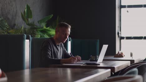 smiling man with works from home in his kitchen using a laptop. remote work and remote learning. remote work during self-isolation in quarantine, man works with financial documents.