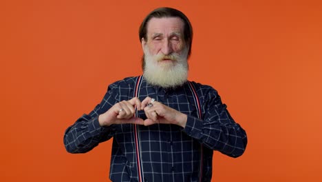 smiling senior man makes heart gesture demonstrates love sign expresses good feelings and sympathy