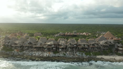 as the sunsets over the mayan jungle, unique village architecture dots the landscape along the shoreline in tulum, mexico