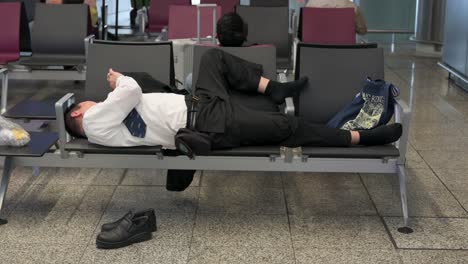 a passenger rests on an airport bench at the arrival hall as he uses his phone for timepass in hong kong international airport