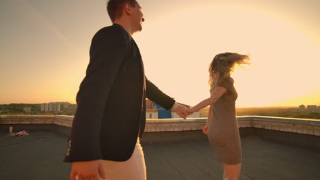 Cute-lovers-laughing-running-on-the-roof-of-the-building-at-sunset-on-the-background-of-the-city-and-hugging-standing-at-the-edge.-Romance-and-love