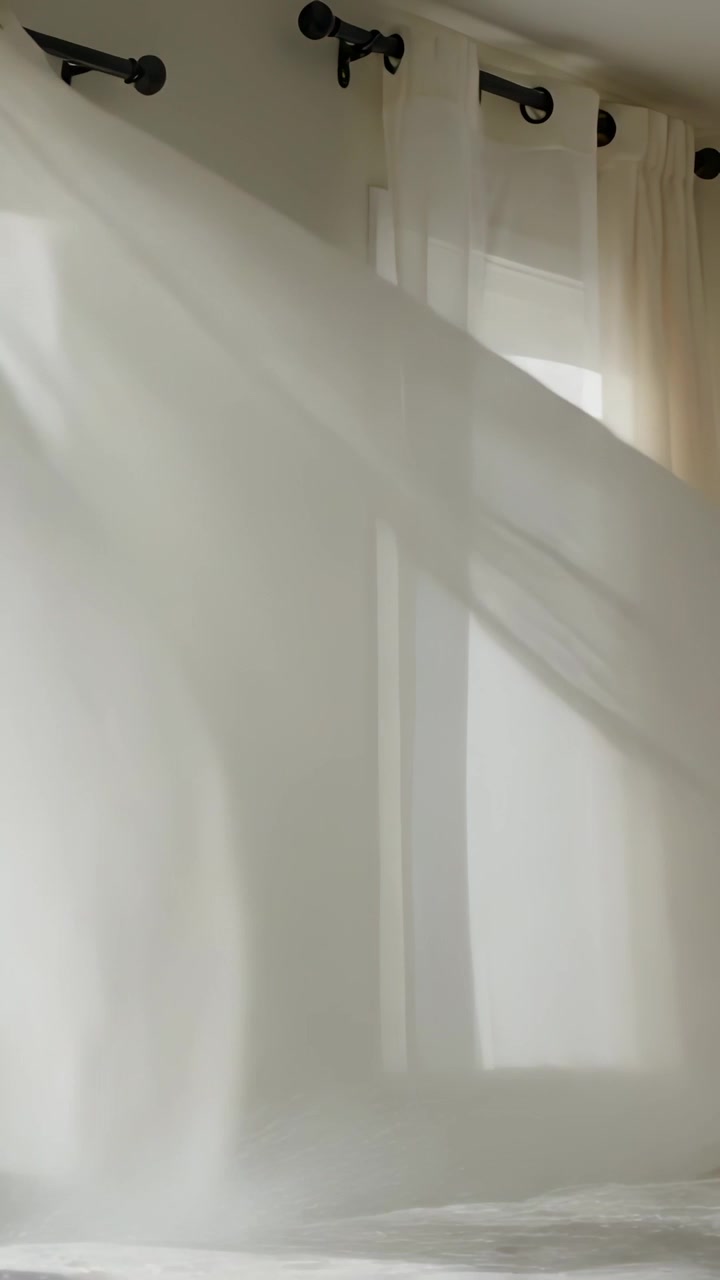 Video verticale: Lenzuolo bianco che ondeggia nella camera da letto, mosso dalla brezza della finestra, rivelando il letto.