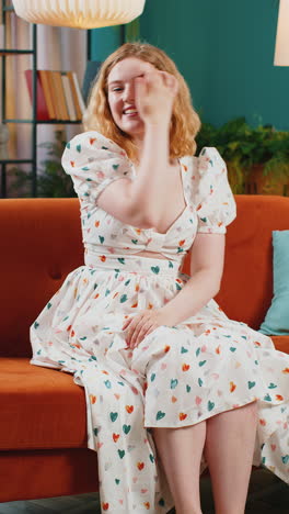 pretty woman smiling friendly at camera waving hands gesturing hello hi greeting at home on sofa