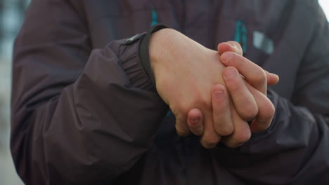 primer plano de las manos juntas en un giro pensativo o un gesto contemplativo, con enfoque en los detalles de la piel y la chaqueta de invierno