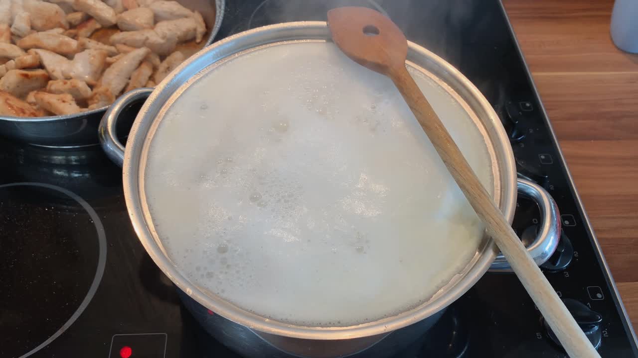 горшок с водой кипит на электрической плите рядом с сковородкой с жареным мясом