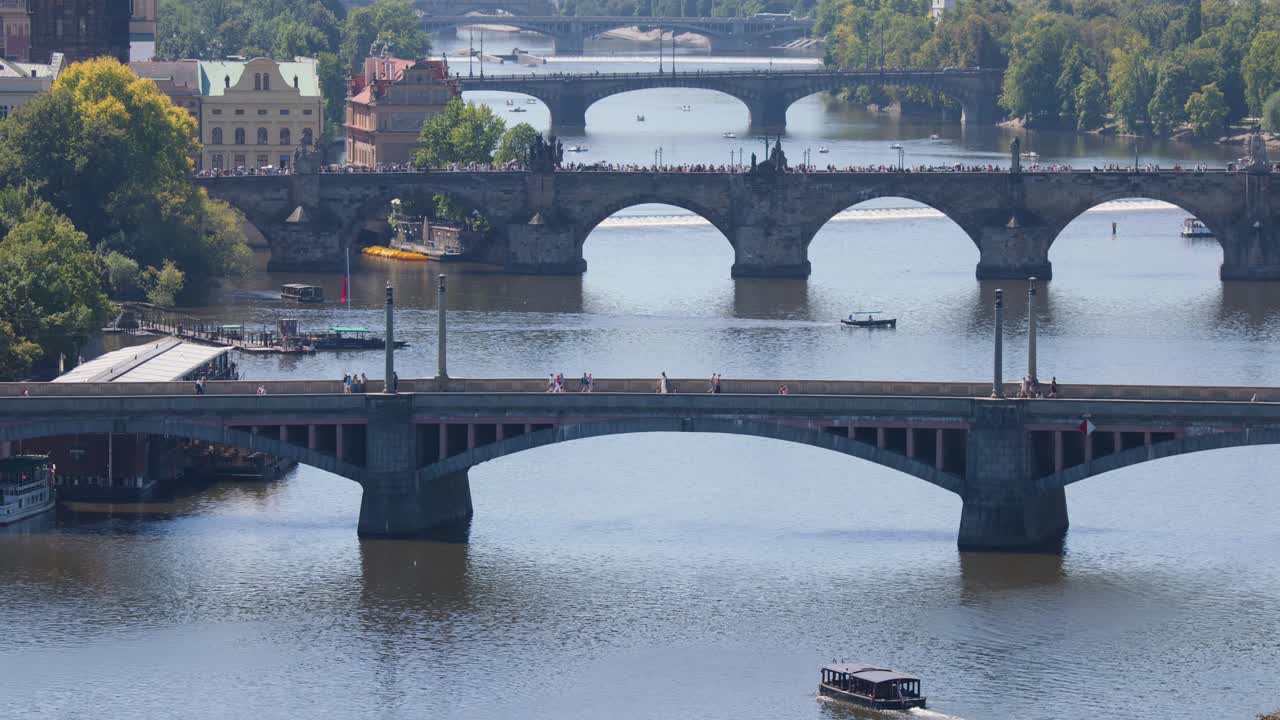 Aerial view of tour boat moving beneath city bridges on sunny summer day in Prague