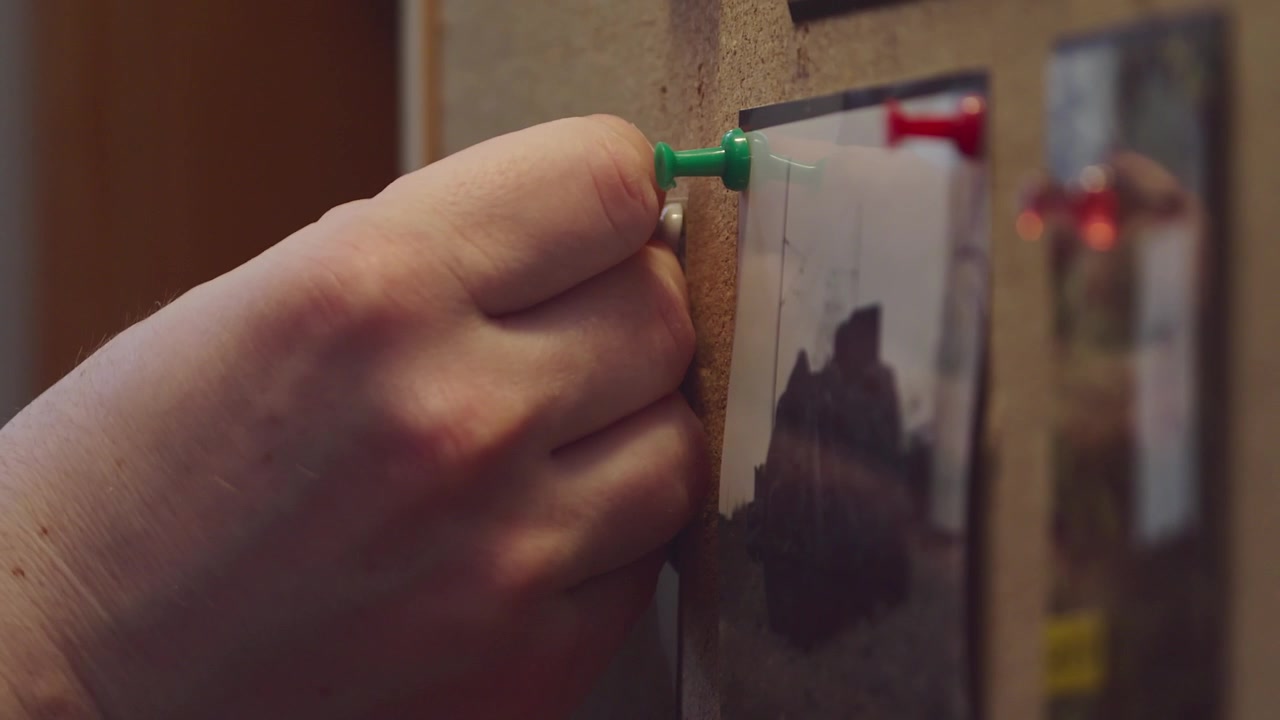 La mano del detective appunta le fotografie alla bacheca delle prove
