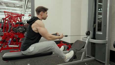 hombre muscular entrena la parte inferior de la espalda en una fila sentada máquina de cable en un centro de fitness moderno