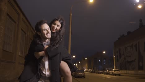 couple dressed in stylish clothes walking down the street celebrating new year, the guy carries the girl over his back