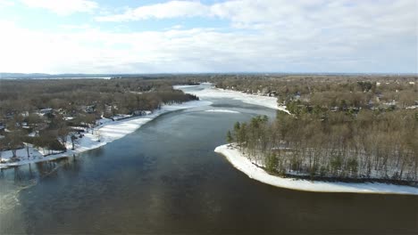 aerial over icy river in winter snow on forested riverbanks