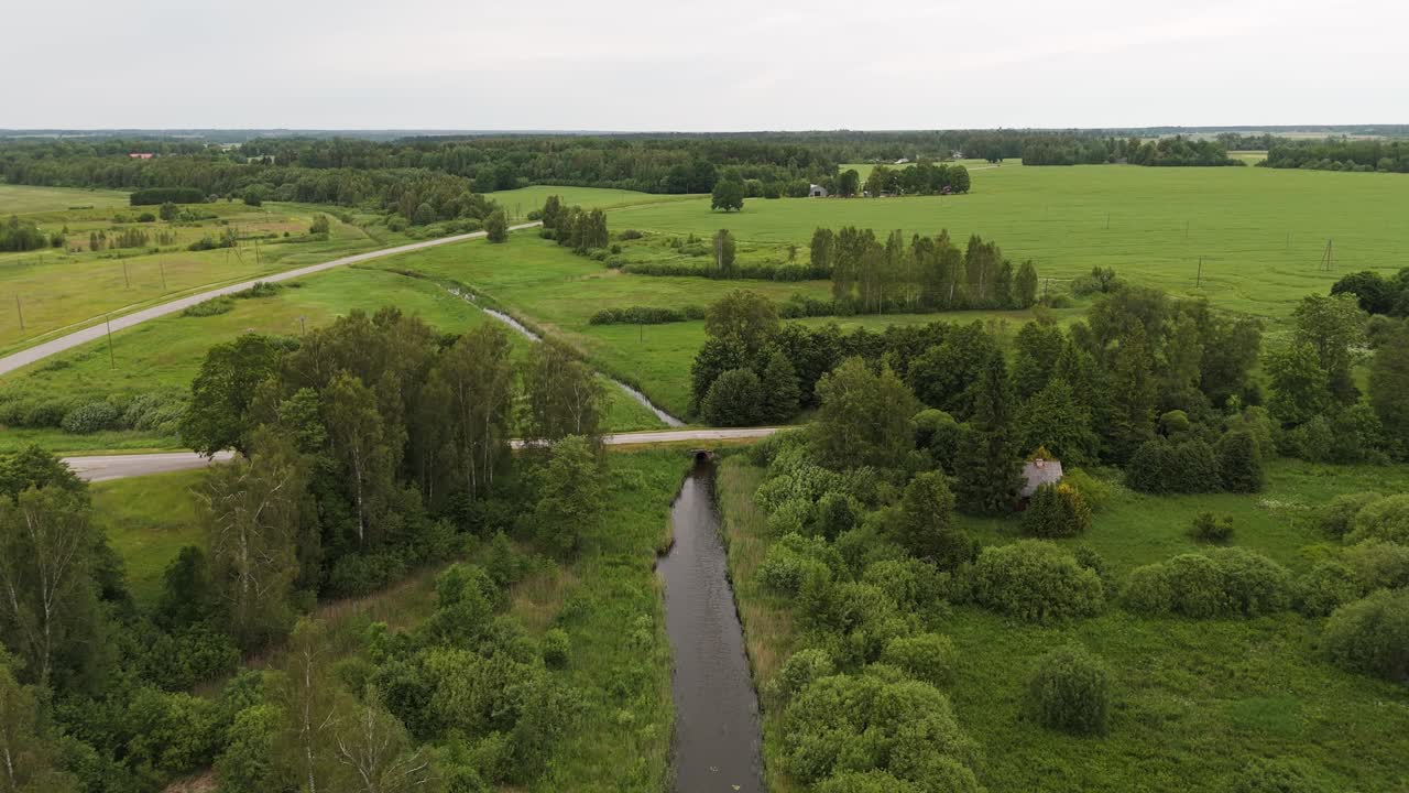 Narrow water stream with bridge and endless green landscape, aerial view