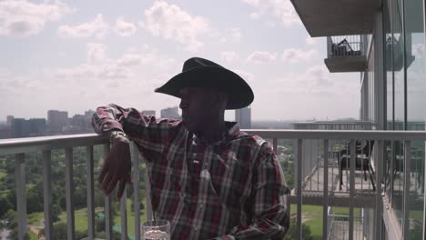 establishing shot of african american male with cowboy hat sitting on balcony