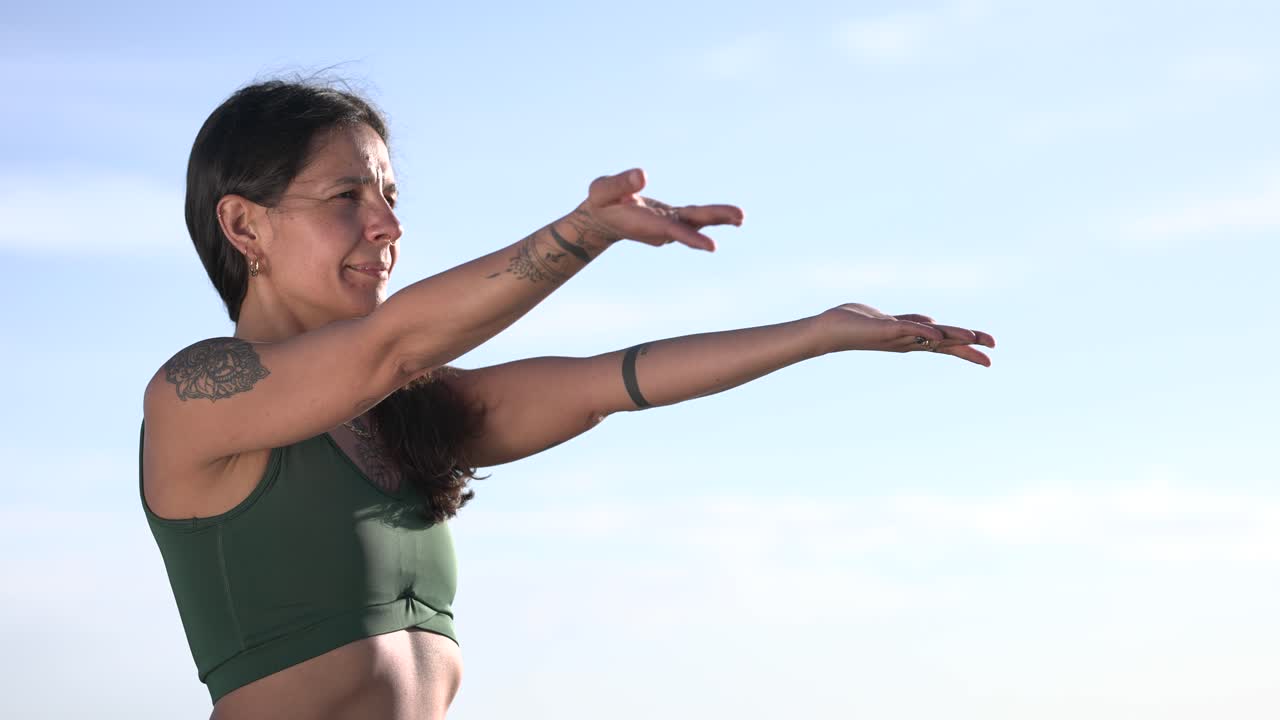 Yoga instructor performing arm stretches against blue sky