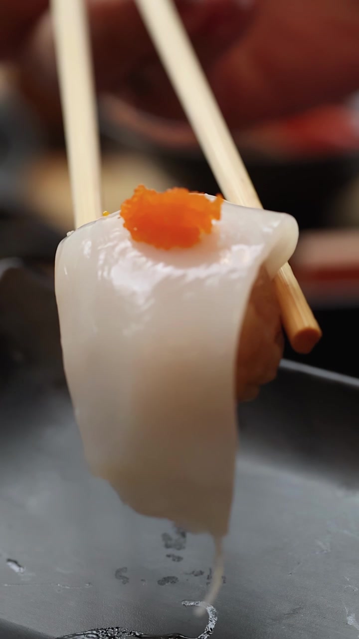 Cận cảnh đũa gắp nigiri mực bóng bẩy có trứng cá trên đĩa tối màu, lấy nét nông