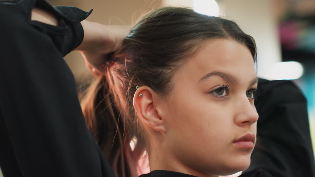 Primo piano ravvicinato del profilo di una studentessa adolescente che si lega i capelli a coda di cavallo in studio, con le mani che fissano i capelli con un elastico, luci bokeh soffuse, espressione concentrata, routine di allenamento prima della lezione di ballo, top nero casual