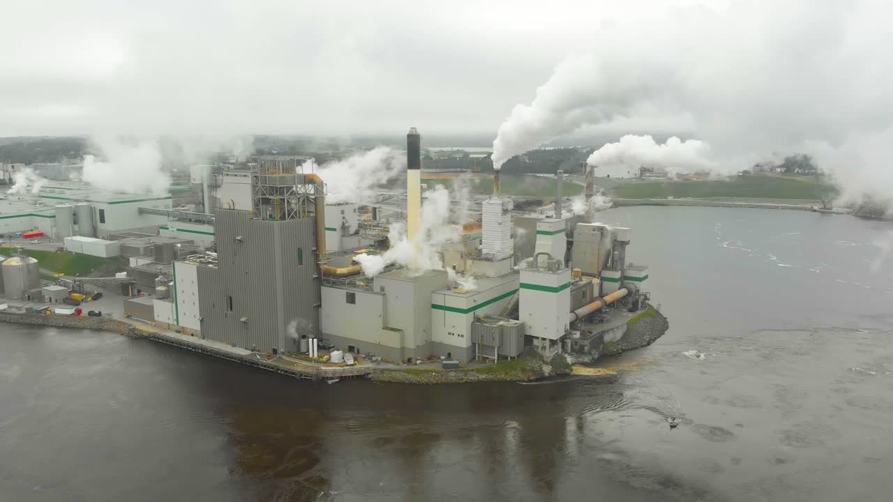 Static aerial shot of the Irving Pulp Factory shooting toxic smoke into the air next to the reversing falls in New Brunswick