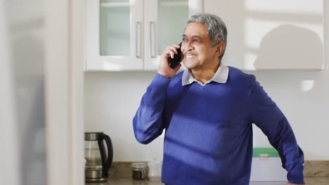 Video-De-Un-Feliz-Hombre-Birracial-Mayor-Hablando-Por-Teléfono-Inteligente-En-La-Cocina,-Sonriendo